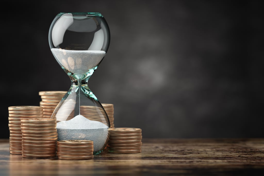 Hourglass with sand running down surrounded by stacks of coins, symbolising the value of time and money management.